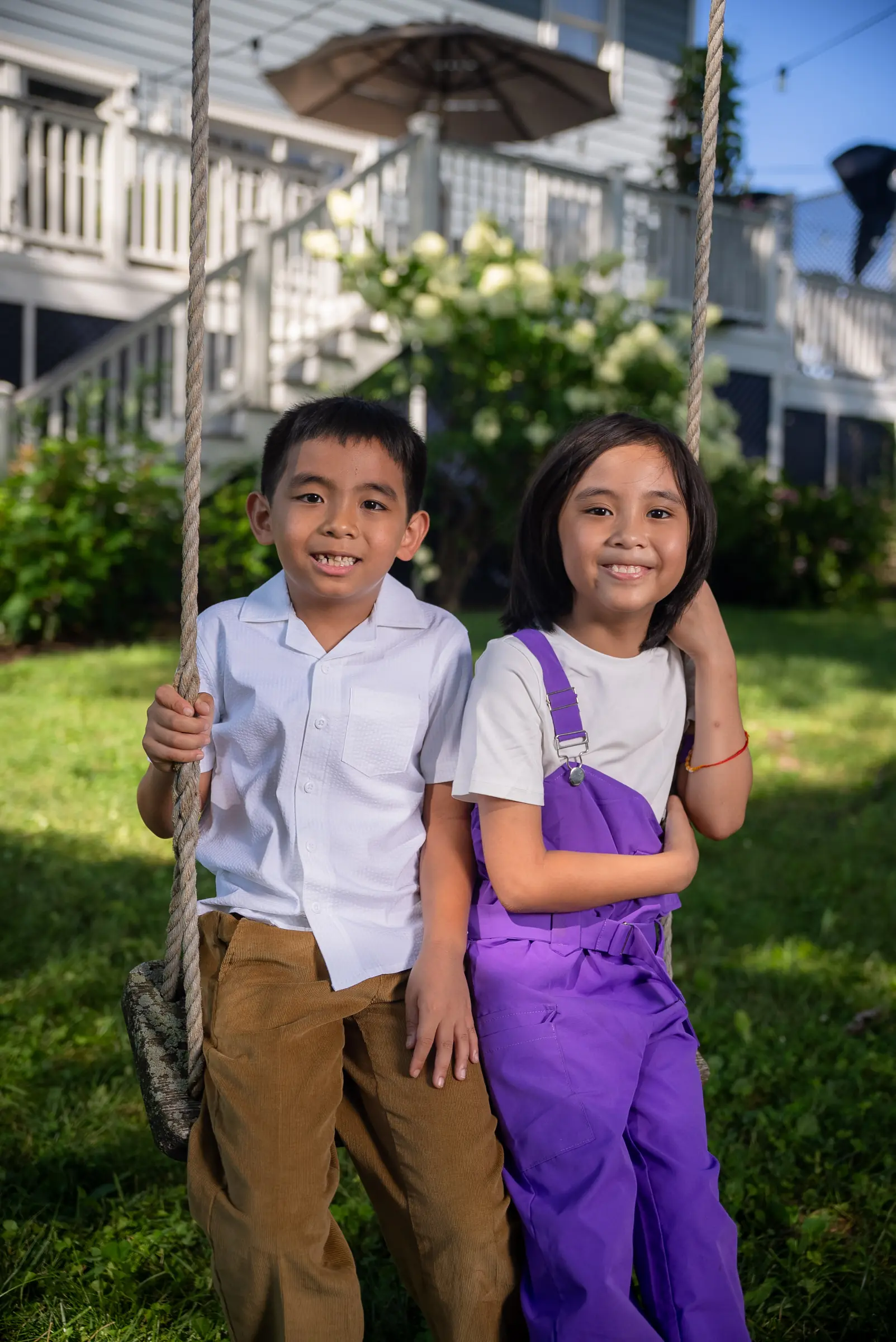 Two young siblings on a garden swing, smiling
